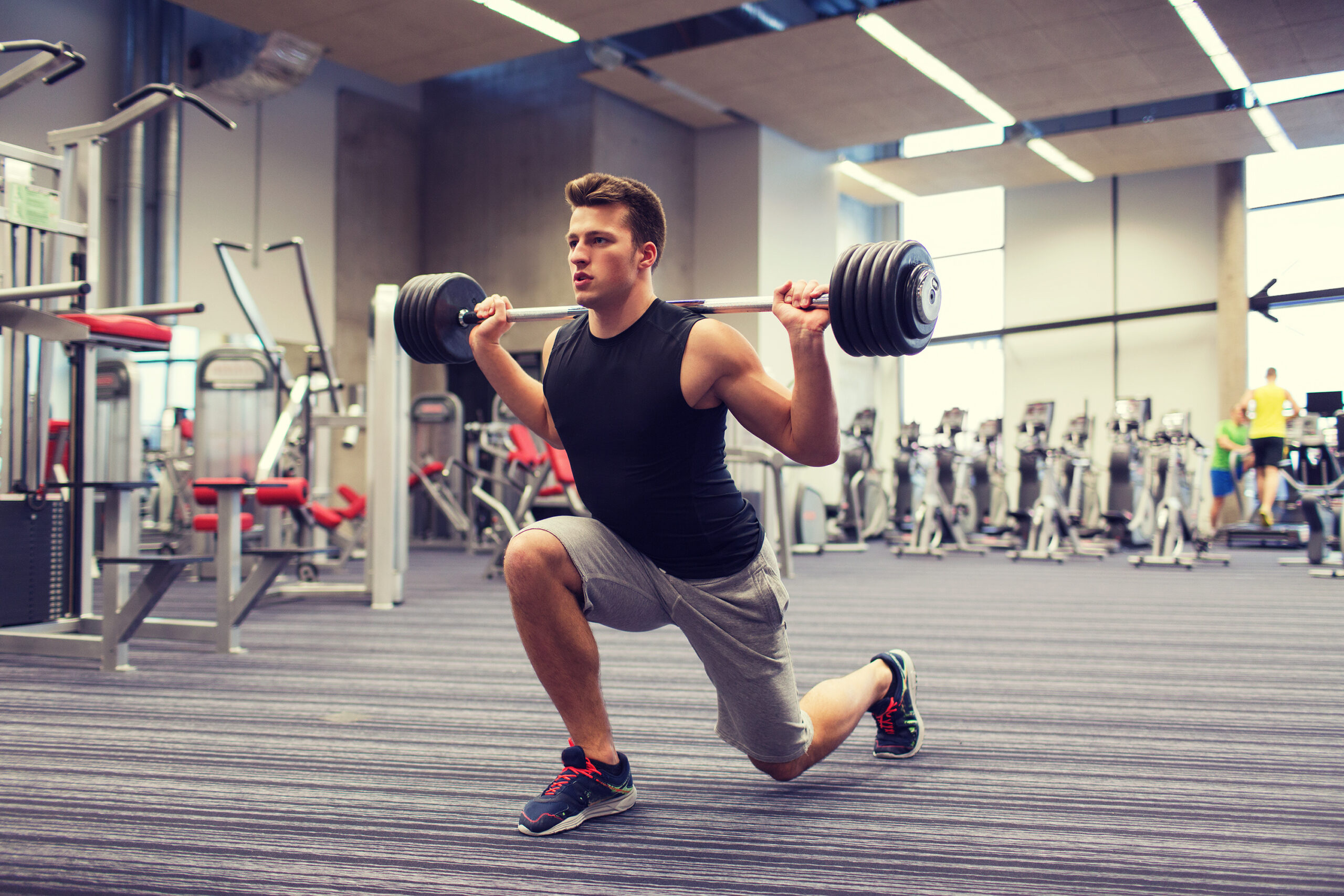 young man flexing muscles with barbell in gym sport, bodybuilding, lifestyle and people concept - young man with barbell flexing muscles and making shoulder press lunge in gym